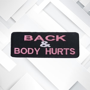 May include: Black embroidered patch with pink lettering that reads "Back & Body Hurts".