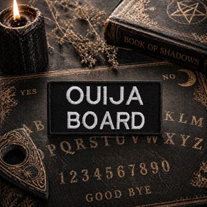 May include: A black Ouija Board patch with white embroidered text reading "OUIJA BOARD" rests on a vintage Ouija board. A lit black candle, a planchette, and a book titled "BOOK OF SHADOWS" are also visible, creating a mystical theme.
