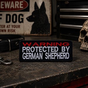 May include: A black and red patch with the text "WARNING PROTECTED BY GERMAN SHEPHERD" sits on a textured surface. A black dog collar, chain, and a "BEWARE OF DOG" sign are in the background.