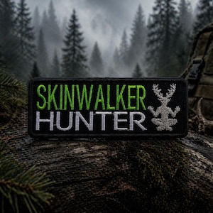 May include: Black rectangular patch with the words "SKINWALKER HUNTER" in green and white lettering. A gray deer-like figure is on the right. The patch is set against a backdrop of a forest and antlers.