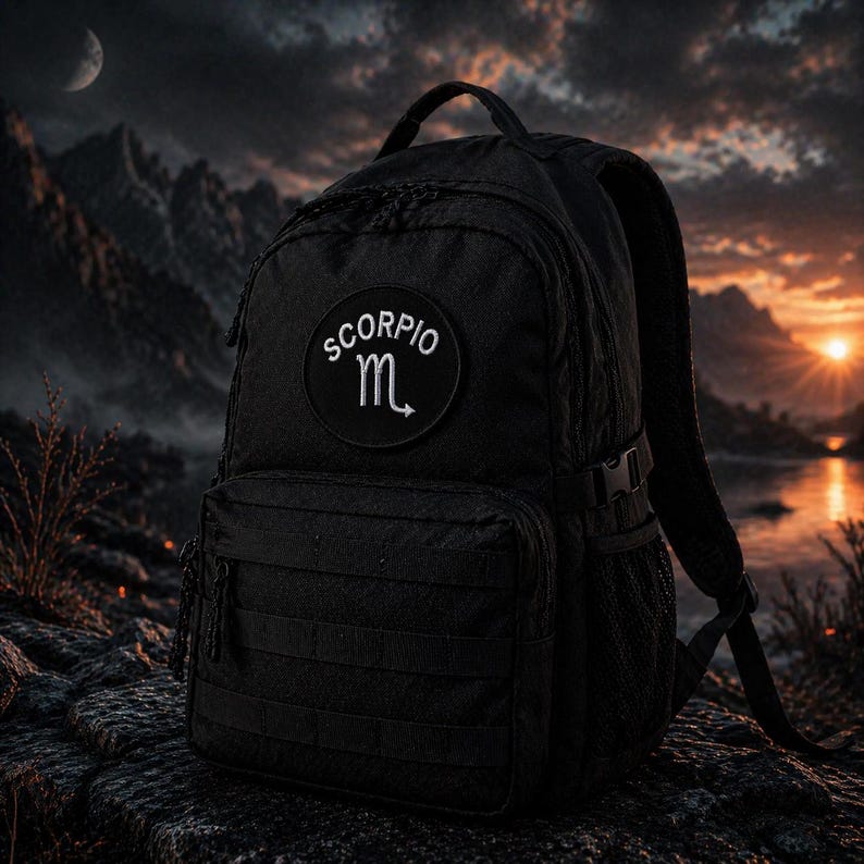 Puede incluir: Mochila negra con un parche que dice "SCORPIO" y un s&iacute;mbolo. La mochila tiene m&uacute;ltiples compartimentos, un asa superior y correas ajustables. El fondo muestra una puesta de sol sobre un lago y monta&ntilde;as.