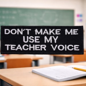 May include: Black rectangular patch with white embroidered text that reads "DON'T MAKE ME USE MY TEACHER VOICE." The patch is in a classroom setting, with a chalkboard, desks, and pencils in the background.