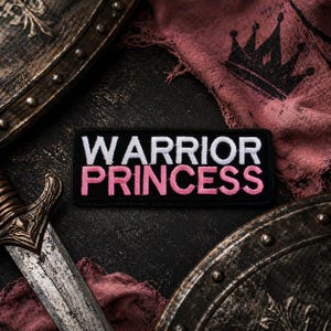 Pode incluir: Um patch preto com as palavras "WARRIOR PRINCESS" em letras brancas e rosa. O patch é cercado por uma espada, um escudo e um pedaço de tecido rosa com um desenho de coroa.