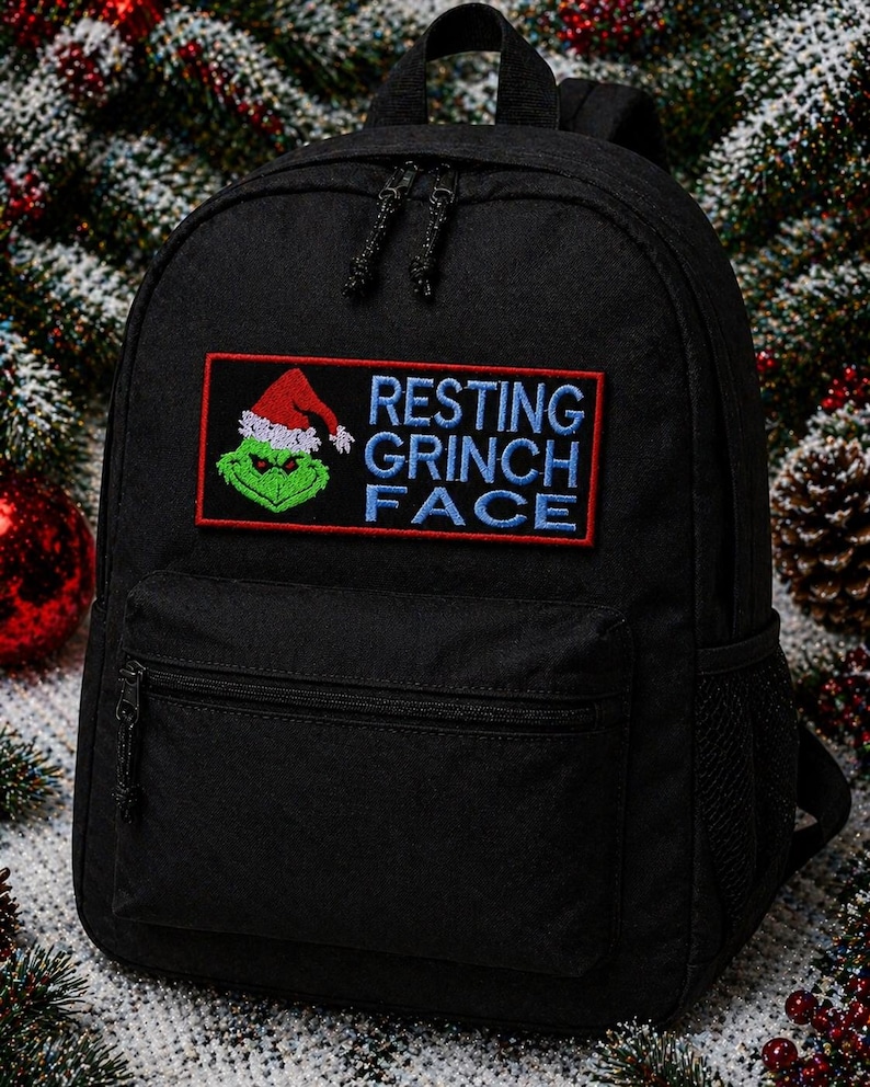 May include: Black backpack with a front pocket and a mesh side pocket. The backpack features an embroidered patch with the Grinch wearing a Santa hat and the words "RESTING GRINCH FACE" in blue and red.