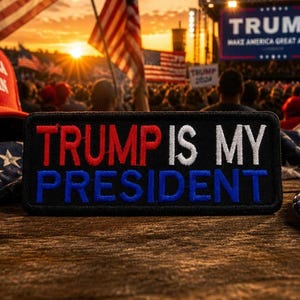 May include: A black patch with the text "TRUMP IS MY PRESIDENT" in red, white, and blue. The patch is on a wooden surface, with a red "AMERICA GREAT AGAIN" hat and an American flag in the background.