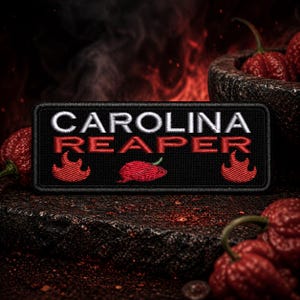May include: A black patch embroidered with the words "CAROLINA REAPER" in white and red. The patch features a red chili pepper and flames. Several red chili peppers are in the background.