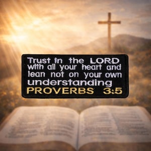 May include: A black rectangular patch with white text that reads "Trust in the LORD with all your heart and lean not on your own understanding PROVERBS 3:5". The patch is set against a blurred background of a cross, a bible, and a sunset.