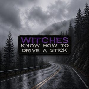 Puede incluir: Parche bordado negro con el texto "WITCHES KNOW HOW TO DRIVE A STICK" en morado y blanco. El parche es rectangular y está colocado sobre un fondo de una carretera sinuosa a través de un bosque.