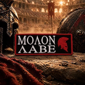 Puede incluir: Parche rectangular negro con las palabras blancas "MOLON LABE" y un casco espartano rojo. El parche se encuentra frente a un telón de fondo de una escena de batalla con cascos y un escudo.