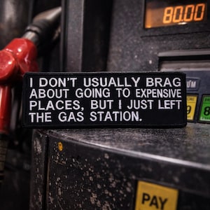 Puede incluir: Parche negro bordado con texto blanco: "I DON'T USUALLY BRAG ABOUT GOING TO EXPENSIVE PLACES, BUT I JUST LEFT THE GAS STATION." El parche está en una gasolinera, con la pantalla de precio mostrando 80,00.