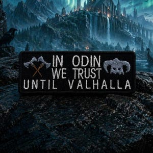 May include: Black rectangular patch with white embroidered text: "IN ODIN WE TRUST UNTIL VALHALLA." Features crossed axes and a ram skull design. Set against a dark, textured background with a fantasy landscape.