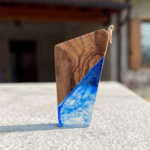 May include: A wooden pendant with a blue and white resin inlay. The pendant has a gold bail and is shaped like a triangle.