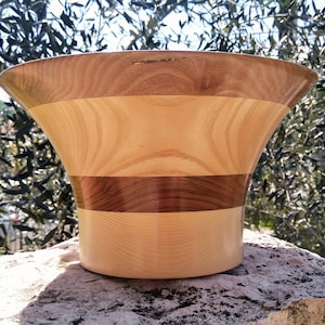 May include: A large wooden bowl with a flared rim and a natural wood finish. The bowl is made of multiple types of wood, creating a striped pattern.