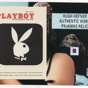 May include: A vintage Playboy magazine cover featuring the bunny logo in black and white. The text "PLAYBOY ENTERTAINMENT FOR MEN" is in red and white. The image also includes text that reads "HUGH HEFNER AUTHENTIC WORN PAJAMAS RELIC".