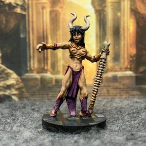 May include: A miniature figurine of a female demon with horns, holding a spiked club. The figure is painted with gold, purple, and flesh tones. The background depicts an ancient temple.