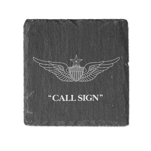 May include: A black slate coaster with a white outline of a pilot's wings and a star. The text "CALL SIGN" is printed below the wings.