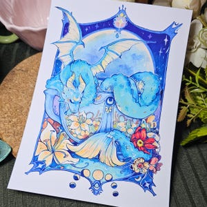 Op de afbeelding: Een blauwe draak die zich oprolt in een theekopje met een bloemenmotief. De staart van de draak is om de buitenkant van het kopje gewikkeld. De achtergrond is donkerblauw met sterren en een maan.