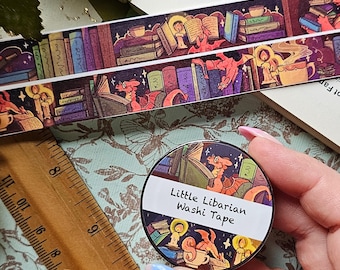 May include: A close-up of a round, black and white sticker with a dragon reading a book. The sticker says "Little Librarian Washi Tape".
