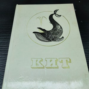 May include: A white book cover featuring a black and white illustration of a whale leaping from the water. The book title, "KIT", is written in gold lettering.