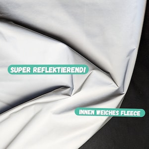 Könnte beinhalten: Ein silberner reflektierender Stoff mit dem Text "SUPER REFLEKTIEREND!" und "INNEN WEICHES FLEECE" darauf gedruckt.