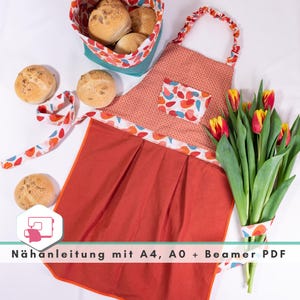 Könnte beinhalten: Eine rote Schürze mit einer weißen und orangefarbenen Tasche mit Muster und einem weißen und orangefarbenen Saum. Die Schürze hat einen gerafften Rock und wird am Hals gebunden. Ein Strauß orangefarbener und gelber Tulpen befindet sich in der rechten unteren Ecke des Bildes. Der Text "Nähnanleitung mit A4, A0 + Beamer PDF" befindet sich am unteren Rand des Bildes.