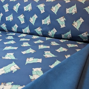 May include: Blue fabric with a repeating pattern of white polar bears wearing teal scarves and holding a small penguin. The fabric is folded over a solid blue fabric.