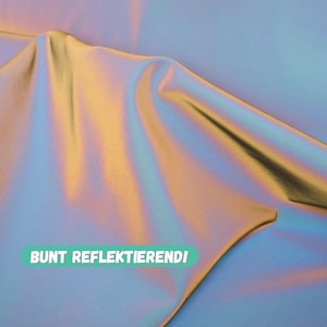 Könnte beinhalten: Nahaufnahme eines schillernden Stoffes. Der Stoff hat eine glatte Textur und reflektiert ein Farbspektrum, darunter Gold, Blau und Lila. Der Text "BUNT REFLEKTIEREND!" ist in einem grünen, abgerundeten Rechteck gedruckt.