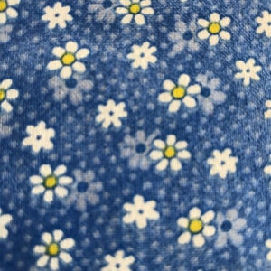 May include: Blue fabric with a white daisy pattern. The daisies have yellow centers.