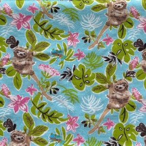 May include: A light blue fabric featuring a repeating pattern of brown sloths hanging from branches, surrounded by green tropical leaves and pink flowers. The design includes various foliage shapes and small white fern-like botanical illustrations.