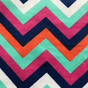 May include: Close-up of a fabric with a chevron pattern. The design features alternating zigzags in white, light teal, pink, navy blue, and orange. The fabric has a textured appearance.