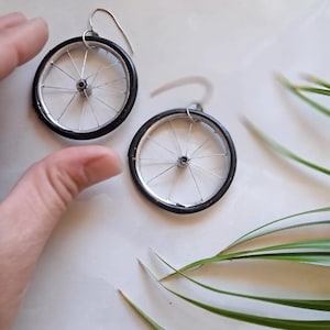 May include: A pair of silver earrings shaped like bicycle wheels with black tyre rims.