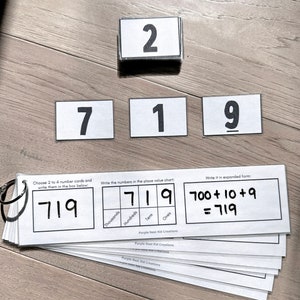 May include: A black and white worksheet with the number 719 written in a box. The number is broken down into its place value components: 700 + 10 + 9 = 719. The worksheet is titled "Purple Nest Kid Creations".