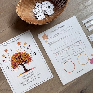 May include: A printable worksheet for teaching rounding numbers. The worksheet features a colorful autumn tree with numbers on the leaves and a number line. The text "The Rounding Tree" and "Find the number. Look next door. Five or higher, add one more. Four or less, let it rest." is included on the worksheet. The worksheet also includes a section for rounding practice with a number line and boxes for placing number cards.