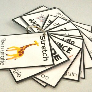 Peut inclure: Un jeu de cartes avec diff&eacute;rents mots et images, dont une girafe, un chat et le mot "stretch". Les cartes sont reli&eacute;es entre elles par un anneau m&eacute;tallique.