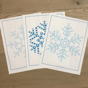 May include: Three printable snowflake templates with a blue and white polka dot design. The snowflakes are on white paper with a blue border. The bottom template has the text "Purple Nest Kid Creations".