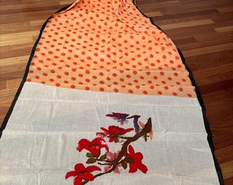 May include: A lightweight scarf with a two-tone design. The top portion features an orange background with red polka dots. The bottom half is white with a floral branch design in red and purple. The scarf has a black border and fringe.