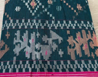 May include: A folded green fabric with a white and gold geometric pattern. The fabric has a pink border.