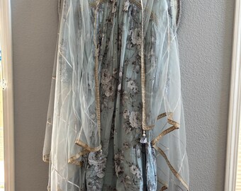 May include: A light blue floral print dress with a matching sheer shawl. The dress features a V-neckline with gold embellishments and a detailed hem. The shawl has gold trim and tassels.
