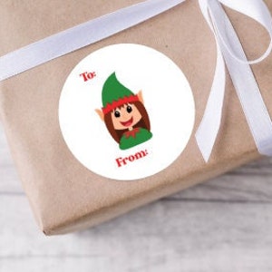 May include: Round white sticker with a cartoon elf illustration. The elf has brown hair, green clothing, and a red hat. The sticker says "To:" and "From:" in black text.