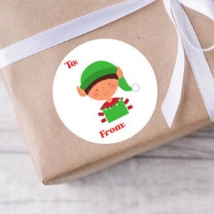 May include: A white round gift tag with a cartoon elf wearing a green hat and red and white striped sweater. The tag says "To:" and "From:" in red text.