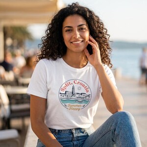 Könnte beinhalten: Ein weißes Kurzarm-T-Shirt mit einer kreisförmigen Grafik, die eine schwarze Linienzeichnung der Skyline von Split, Kroatien, eine Sonne, blaue Wellenlinien und den Text Split, Croatia und Summer Happy in roter und goldener Schrift zeigt.