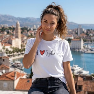 Può includere: Una t-shirt bianca a maniche corte con la scritta I heart Split in caratteri neri, un simbolo di cuore rosso e un piccolo disegno a linee nere che raffigura la silhouette di uno skyline urbano stampato sul davanti.