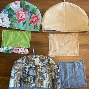 Peut inclure: Ensemble de quatre housses de théière. Une housse est verte à imprimé floral rose et blanc, une est beige, une est marron à imprimé cheval blanc et une est bleue à imprimé cheval blanc. L'ensemble comprend également trois dessous de plat assortis. Un est vert, un est beige et un est bleu.