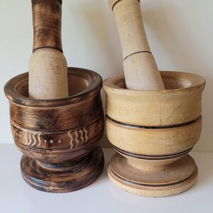 May include: Two wooden mortars and pestles. One mortar is dark brown with a carved design and the other is light brown with black stripes. Both mortars have a round base.