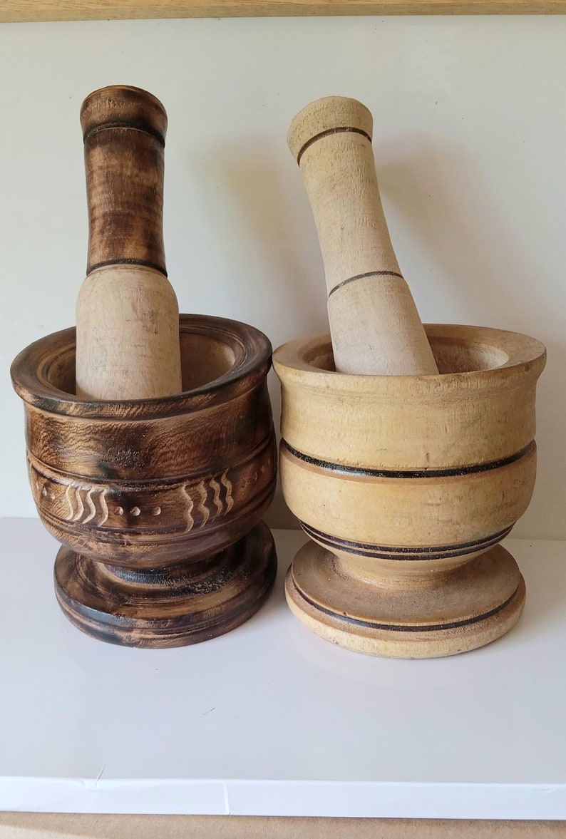 May include: Two wooden mortars and pestles. One mortar is dark brown with a carved design and the other is light brown with black stripes. Both mortars have a round base.