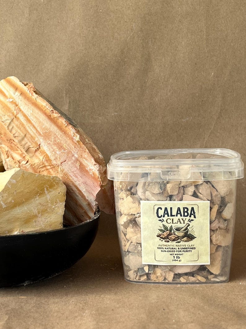 Puede incluir: Un recipiente de pl&aacute;stico transparente lleno de peque&ntilde;os trozos irregulares de arcilla Calaba, etiquetado con el texto 'CALABA CLAY, AUTHENTIC NATIVE CLAY, 100% NATURAL & UNREFINED, SUN-DRIED FOR PURITY, NET WEIGHT 1 lb (454 g)', junto a un cuenco negro de arcilla.