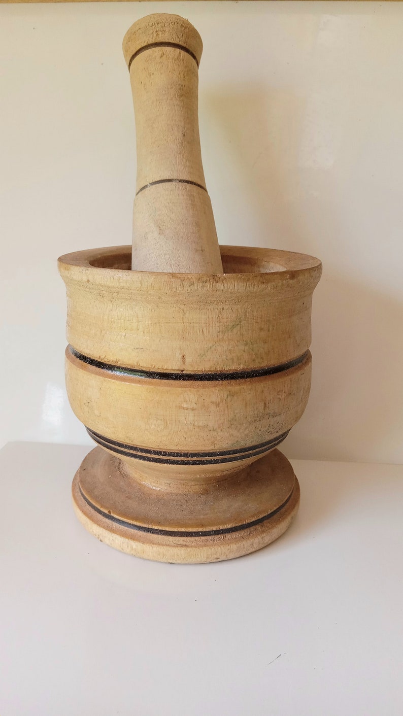 May include: A wooden mortar and pestle with a light brown finish and black accents. The mortar has a wide base and a rounded bowl. The pestle is cylindrical with a rounded top.