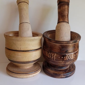 May include: Two wooden mortars and pestles, one with a natural wood finish and the other with a dark brown stain. Both have a carved design around the top.