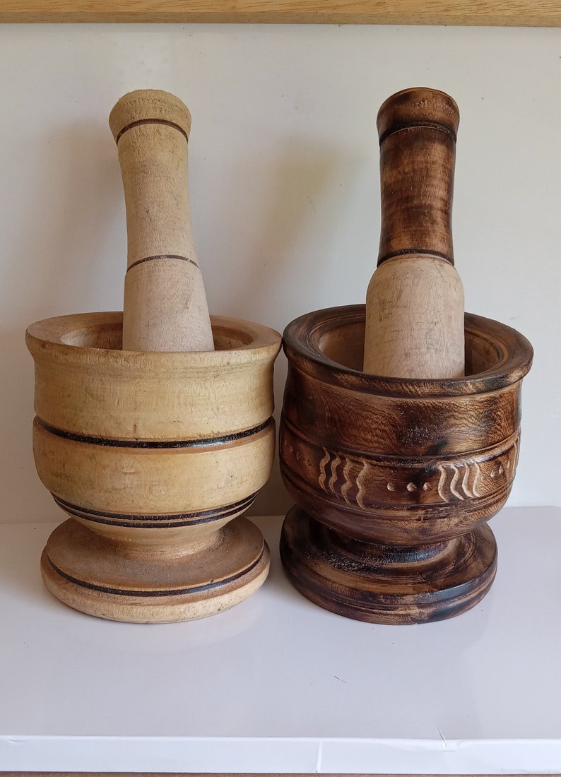 May include: Two wooden mortars and pestles, one with a natural wood finish and the other with a dark brown stain. Both have a carved design around the top.