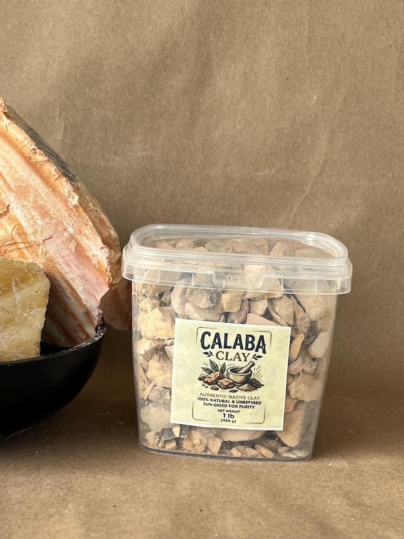 Puede incluir: Un recipiente de pl&aacute;stico transparente lleno de trozos de arcilla beige y marr&oacute;n. La etiqueta dice Calaba Clay, Authentic Native Clay, 100% Natural & Unrefined, Sun-Dried for Purity, Net Weight 1 lb (454 g). A la izquierda hay una roca grande, texturizada y de color beige.